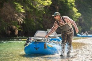 Guide pulling fishing raft boat with seats along river shoreline, Patagonia