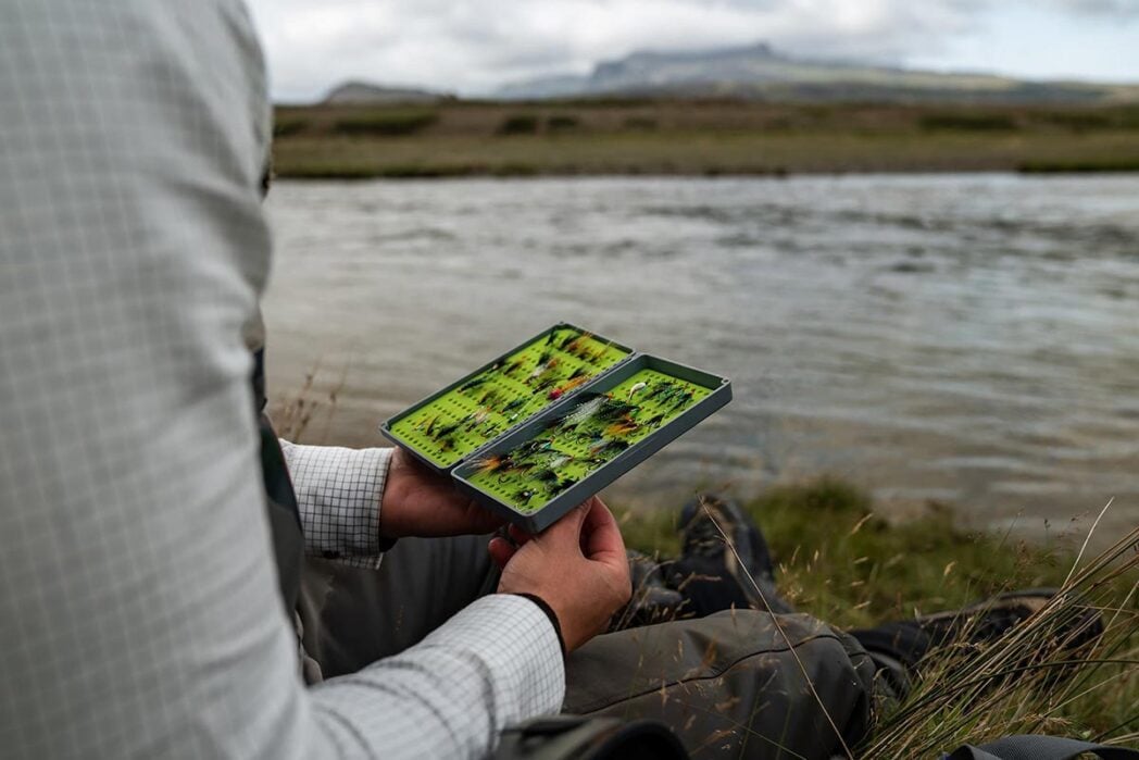 Angler looking at fly box by river