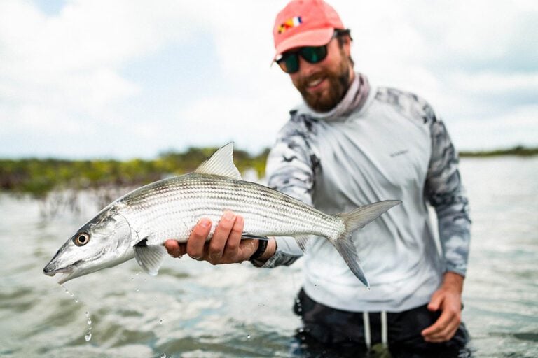 Angler in waist deep water holding bonefish caught fly fishing in the Bahamas around Abaco island