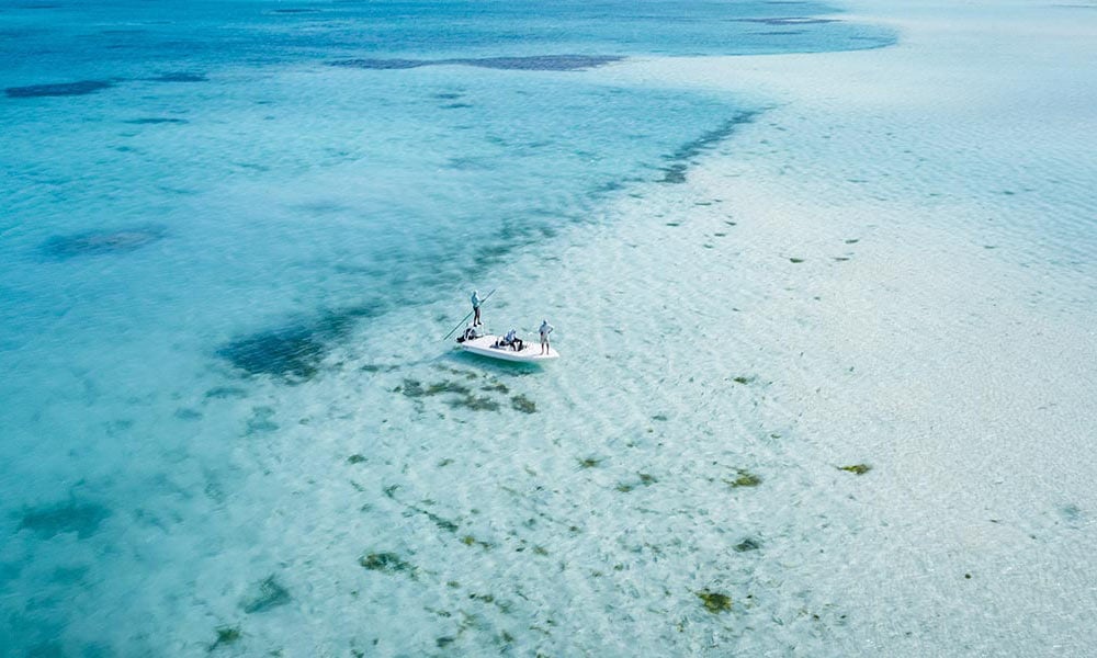 Skiff boat with anglers drifting across flats over turquoise waters