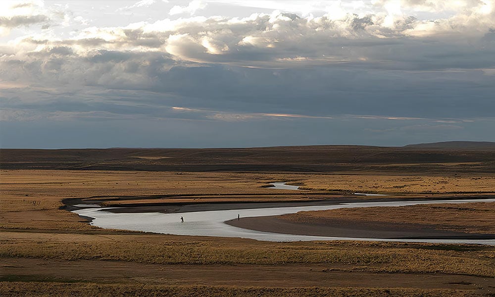 Windswept landscape of river in Tierra del Fuego in Argentina, with anglers fishing for sea-run brown trout