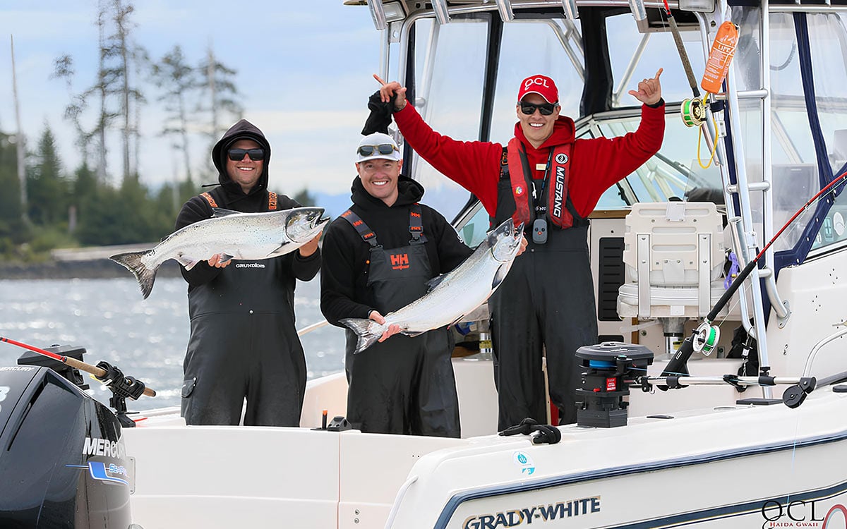 Smiling guests and guide hold up coho salmon caught from boat in Haida Gwaii waters on West Coast of BC Canada