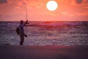 Salt water fly fishing angler in sunset casting from beach into Atlantic Ocean - West Africa, Gabon
