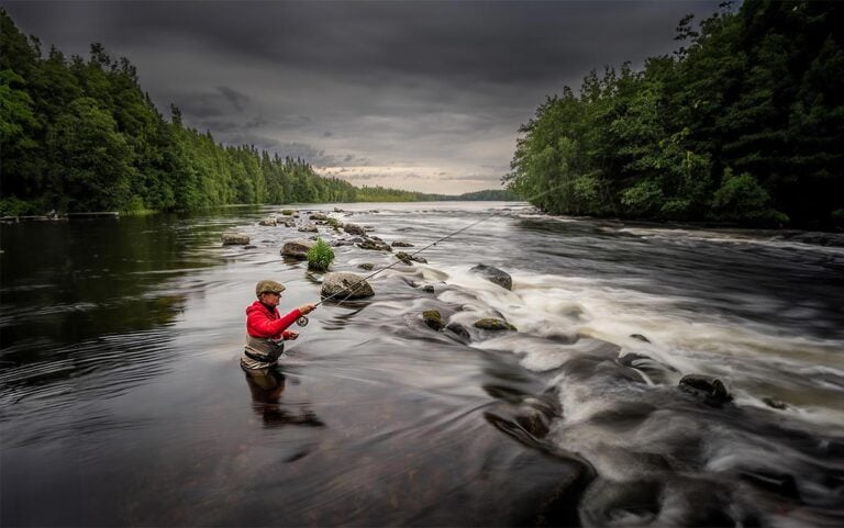 Slow exposure shot of angler in river in Finland, fishing rapids for brown trout