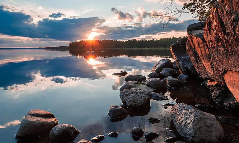 Still lake in Finland in sunset, with rocky shoreline and forest