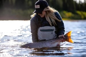Female angler in waist deep water releasing Atlantic salmon back into water on Canada's east coast
