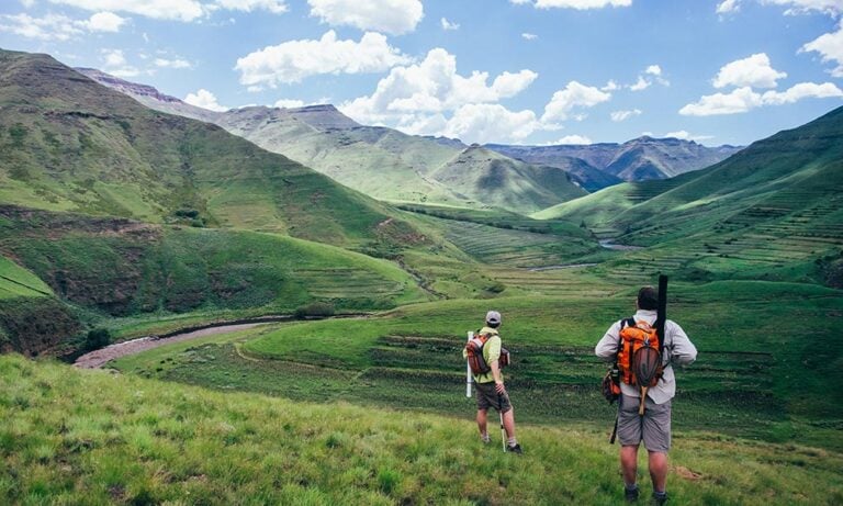 Lush green valley and hills in Lesotho, Africa - two anglers hiking to look for productive waters