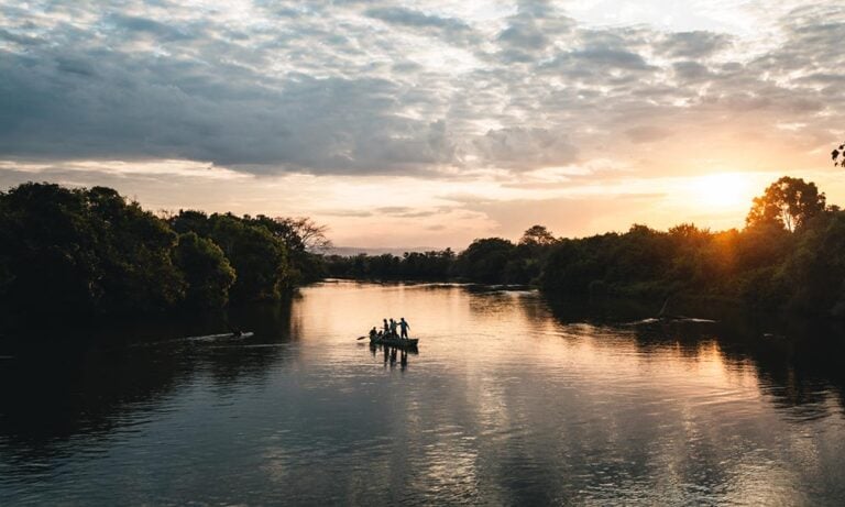 Boat with 3 people floating down river in Tanzania at dusk
