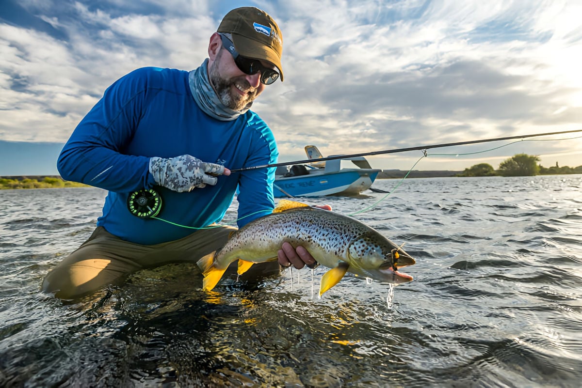 Angler holding trout caught on large river in northern Patagonia, Argentina, with drift boat in background